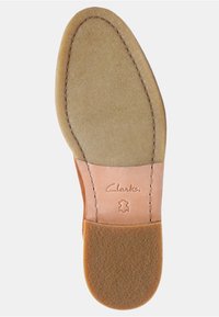 Semelle intérieure en suède marron avec forme courbée, logo Clarks embossé au talon, texture douce et dos en cuir beige.