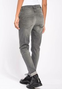 Šedé džíny s úzkým střihem, se zadními kapsami a manžetami na nohavicích. V páru s černými šněrovacími botami.