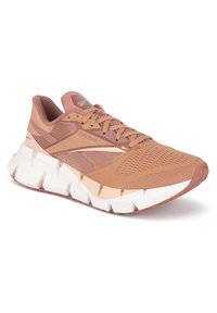 Bežecká obuv Reebok v broskyňovom ružovom odtieni s vrchnou časťou z mesh materiálu, vycpaným golierom a kontrastnou bielou medzi podrážkou. Obsahuje textúrované akcenty a šnúrky.