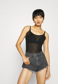 Must mustas õhukesed rihmad, kolmnurkse lõikega, koos kõrge vöökohaga hallide denimsügiseste pükste ja friteeritud servadega.