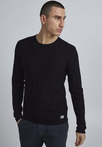 Zwarte lange mouwen shirt met een ronde halslijn, gemaakt van textuurstof. Heeft minimale branding op de onderste zoom en een aansluitende pasvorm.