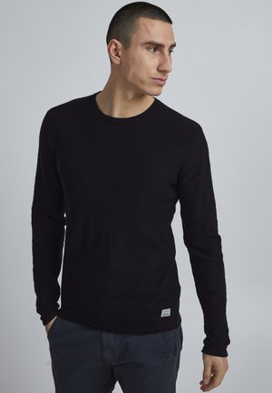 Zwarte lange mouwen shirt met een ronde halslijn, gemaakt van textuurstof. Heeft minimale branding op de onderste zoom en een aansluitende pasvorm.