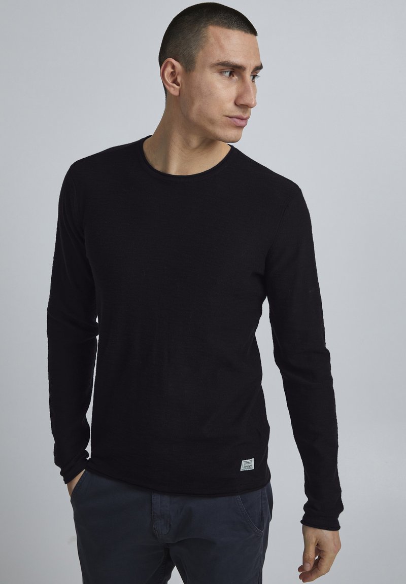 Zwarte lange mouwen shirt met een ronde halslijn, gemaakt van textuurstof. Heeft minimale branding op de onderste zoom en een aansluitende pasvorm.