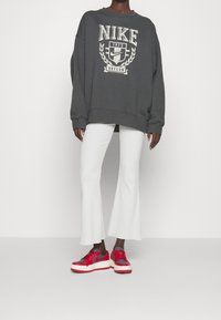 Mörkgrå oversized sweatshirt med "NIKE"-logotyp, vita ribbade utställda byxor och röda och grå sneakers med tjocka vita sålar.