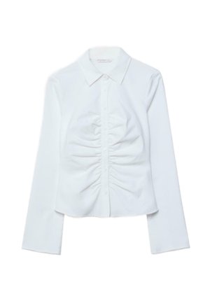 Bela srajca z dolgimi rokavi, z gumbi na sprednji strani, z izrezom v obliki konice in gubami vzdolž sprednjega sredinskega dela.