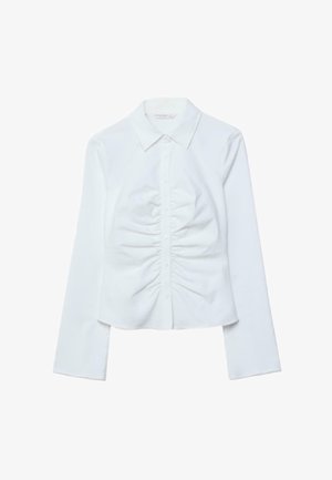 Bela srajca z dolgimi rokavi, z gumbi na sprednji strani, z izrezom v obliki konice in gubami vzdolž sprednjega sredinskega dela.