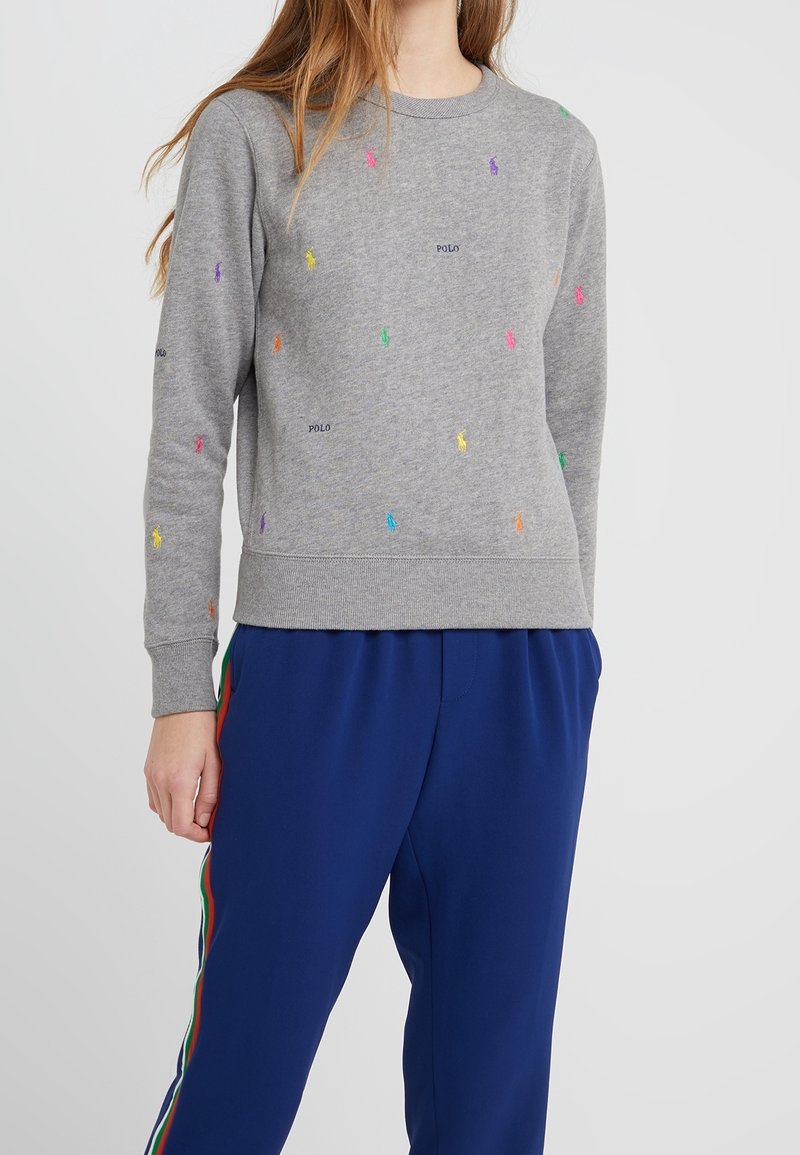 Grå sweatshirt i bomull med flerfärgade broderade logotyper utspridda över ytan. Ribbad muddar och nederkant.