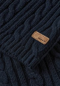 Suéter de punto azul marino con un patrón de trenzas, puños acanalados y una etiqueta de cuero marrón con texto en relieve. Textura de lana suave.