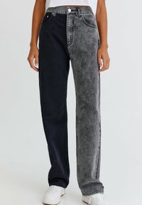 Jeans bicolor que presentan un lado azul oscuro y un lado gris desgastado. Elaborados en denim con un corte recto y un diseño estándar de cinco bolsillos.