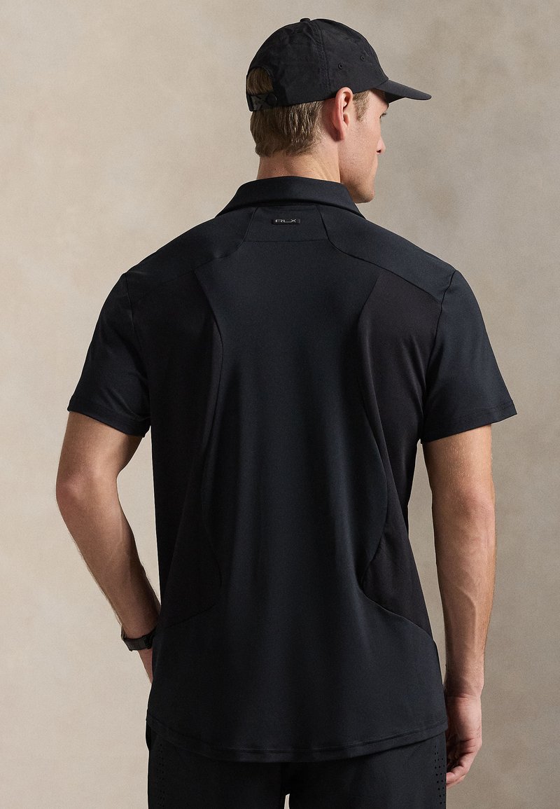 Μαύρο κοντομάνικο πόλο με δομημένο σχεδιασμό, που διαθέτει πλαϊνές πάνελ από δίχτυ, κλασικό γιακά και διακριτικό λογότυπο στην πλάτη.