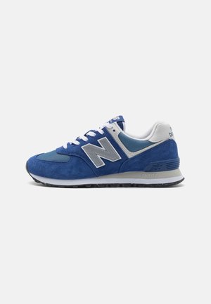 Blauer und weißer New Balance Sneaker mit Wildleder- und Mesh-Obermaterial, Schnürverschluss und gepolsterter Sohle auf weißem Hintergrund.