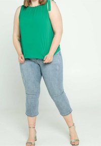 Top verde senza maniche con scollatura plissettata e lacci laterali, abbinato a jeans capri leggeri blu chiaro e sandali verde con cinturini.
