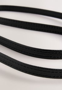 Schwarze synthetische Riemen mit glatter Oberfläche und abgesteppten Kanten, flach in einer geschwungenen Anordnung auf hellem Hintergrund liegend.