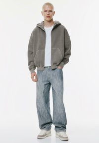 Gray zip-up hoodie over a light t-shirt, paired with light blue striped wide-leg jeans and white shoes with gray accents.