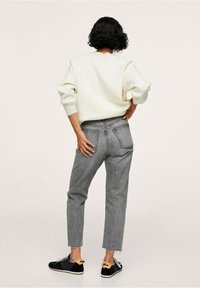 Sudadera crema con mangas raglán, jeans grises de cintura alta con dobladillo desgastado y zapatillas negras con detalle amarillo en el talón.