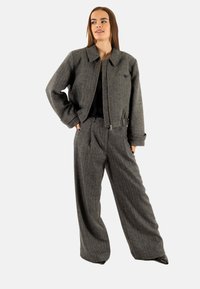 Grijze wollen jas met een kraag en ritssluiting, gecombineerd met grijze hoogliggende wijde broek. Beide hebben subtiele texturen.