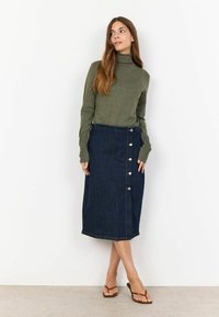 Un pulover verde cu guler înalt, asortat cu o fustă midi din denim albastru, având un detaliu cu butoane pe lateral și croială dreaptă; plasat pe un fundal alb.