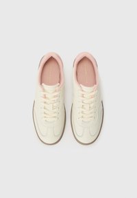 Sneakers bianchi con esterno in pelle liscia, fodera interna rosa, lacci piatti e suole in gomma con dettagli in marrone chiaro e cuciture.
