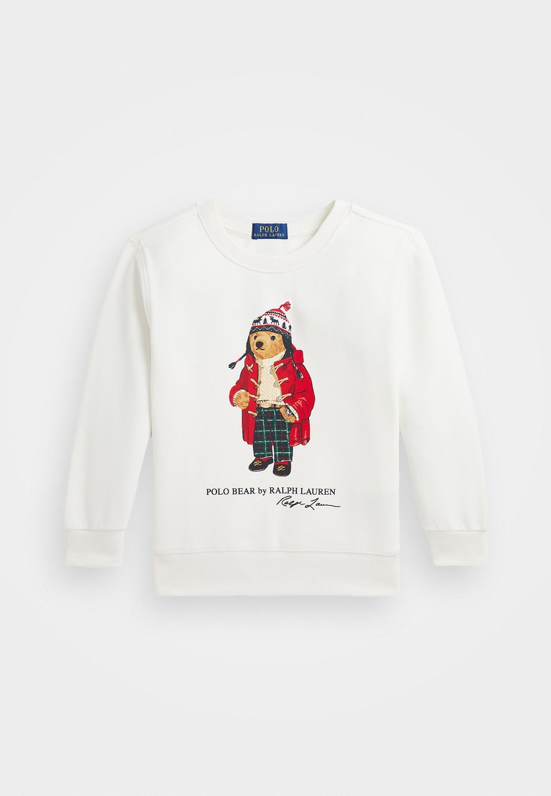 Bijela dukserica sa grafikom medvjeda u crvenom kaputu, hlačama s uzorkom u zelenoj boji i šeširom s pom-pomom. Ispod je prikazan logotip branda.