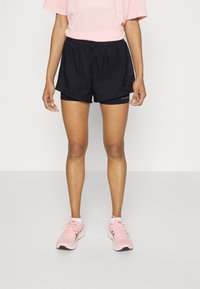 Czarne spodenki do biegania z elastycznym pasem, wykonane z lekkiego materiału, z logo po boku. Połączone z jasnoróżowymi butami sportowymi.