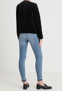 Svart, plysch bomberjacka med ribbad fåll, ihop med ljusblå skinny jeans med fransade vristhällor och svarta loafers.