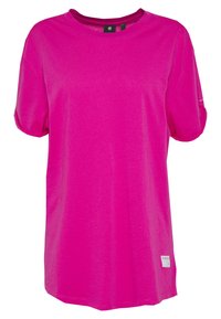 T-shirt rose vif à manches courtes, col rond, avec des manches légèrement retroussées et une petite étiquette blanche près de l'ourlet inférieur.