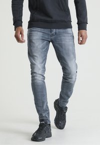 Light blue denim jeans with a slim fit, worn with a black hoodie and black sneakers featuring textured uppers and thick soles.