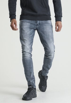 Vaqueros de denim azul claro con un corte ajustado, combinados con una sudadera negra y zapatillas negras con parte superior texturizada y suelas gruesas.
