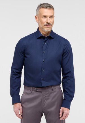 Marineblaue Langarmbluse mit Button-Down-Kragen, ausgestattet mit einer glatten Textur und dezentem Glanz, kombiniert mit grauen Hosen.