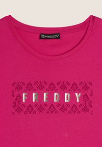 Camiseta de algodón fucsia con escote redondo y la palabra "FREDDY" en dorado metálico, rodeada de un patrón decorativo de damasco.