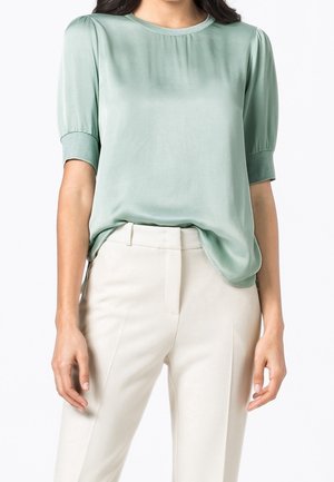 Blusa verde menta a maniche corte in un tessuto leggero e morbido. Collo rotondo con dettagli arricciati sulle spalle. Abbinata a pantaloni chiari.