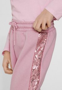 Helle rosa Jogginghose mit einem elastischen Bund und einem Kordelzug sowie einem Seitenpanel, das mit glänzenden rosa Pailletten verziert ist.