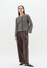 Giacca in tweed grigia e bianca con texture, maniche lunghe e scollatura rotonda, abbinata a pantaloni a gamba larga in velluto a coste marroni e ballerine nere a punta.