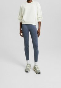 Ljus beige sweatshirt med raglanärmar, kombinerad med mörkblå leggings och grå sneakers, vita ankelsockor. Slät tygtextur.