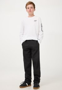 T-shirt bianca a maniche lunghe in cotone con stampa grafica sul petto e pantaloni neri in cotone; sneakers nere con suola in gomma.