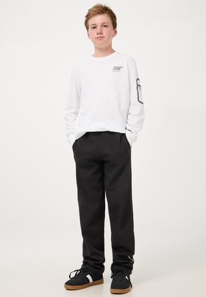 T-shirt bianca a maniche lunghe in cotone con stampa grafica sul petto e pantaloni neri in cotone; sneakers nere con suola in gomma.