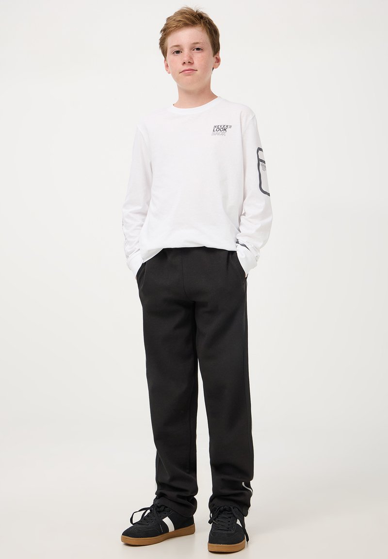 T-shirt bianca a maniche lunghe in cotone con stampa grafica sul petto e pantaloni neri in cotone; sneakers nere con suola in gomma.