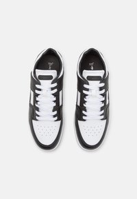 Baskets noires et blanches avec une tige en cuir lisse, une boîte à orteils perforée et des lacets blancs. Elles présentent une bande texturée et un détail logo.