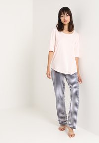 Lichtroze top met korte mouwen en een ronde hals, gecombineerd met marineblauwe en witte gestreepte broek. Zachte stof, losse pasvorm en een casual ontwerp.