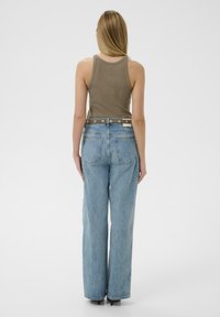 Világosbarna bordázott trikó felső, világoskék, magas derekú, bő fazonú farmernadrággal párosítva, amely gombdíszítéssel és hátsó zsebekkel rendelkezik.