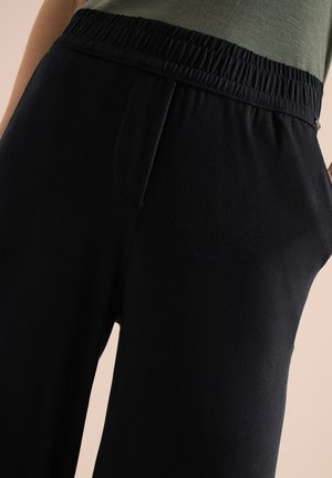 Primer plano de pantalones con cintura elástica negra usados con una blusa verde, destacando la textura de la tela y los detalles de la cintura.