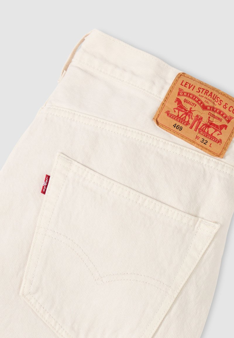 Jean blanc Levi's plié pour montrer la poche arrière et la marque en cuir marron clair avec taille 32, numéro de style 469.