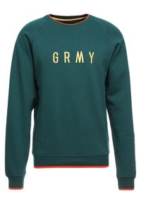 Zielona bluza z okrągłym dekoltem z złotym napisem "GRMY", z kontrastującymi pomarańczowymi akcentami na mankietach i hemie. Miękka tekstura, casualowy design.