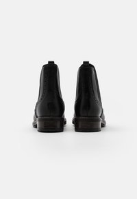 Botines de cuero negro con diseño de brogue, con una textura suave, tacones cuadrados cortos y tiradores en la parte posterior para facilitar su uso.