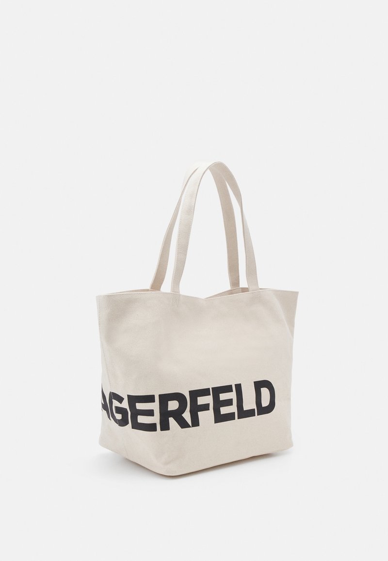Beżowa torba z płótna z dwiema rączkami i dużym czarnym napisem częściowo widocznym "AGERFELD" z przodu.