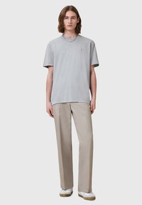 T-shirt grigia a maniche corte con una texture liscia, abbinata a pantaloni beige chiaro e sneakers bianche con suola texturizzata. Collana in argento.