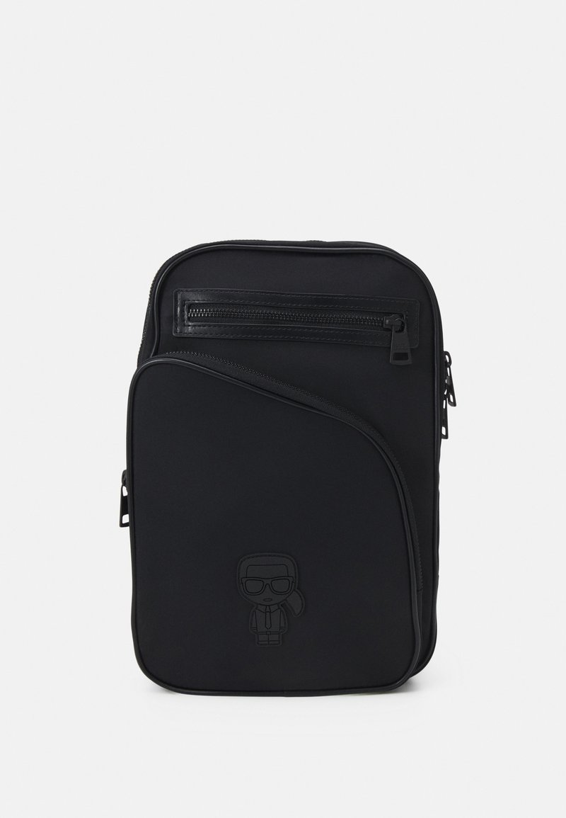Black backpack made of smooth material, featuring a front zip pocket, curved design, and embossed character detail on the lower front.