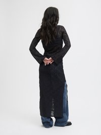 Vestido longo de renda preta com mangas longas, corpete justo e fendas laterais; combinado com jeans de denim azul soltos e sapatos pretos.