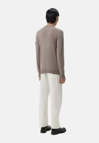 Ljust brunt stickat tröja med rund halsringning, långa ärmar och ribbade manschetter, kombinerad med vita rak ben-byxor och svarta skor.