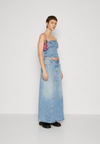 Haut en denim court et jupe longue en bleu clair ; présente une coupe droite, une texture délavée et un sac à main rose. Des bottines noires à la cheville complètent le look.